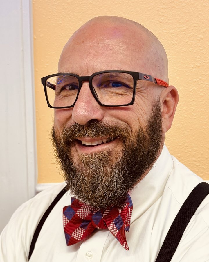 Rev. Dr. Craig D. Greatman, smiling, in glasses, a white shirt and a red checked bow tie